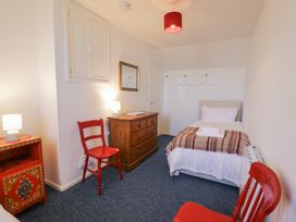 A bedroom with a single bed a wooden dresser two red chairs a red nightstand with a lamp and two hangers on a wall at Pen Y Bryn Bach in Harlech