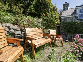 Wooden outdoor benches in a garden area with stone wall greenery flowers and part of a stone cottage at Pen Y Bryn Bach in Harlech
