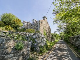 A narrow road with stone walls and a stone house on the left surrounded by trees and greenery at Pen Y Bryn Bach in Harlech