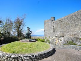 A statue of a rider on a horse on a grassy roundabout near a stone castle wall with a clear blue sky at Pen Y Bryn Bach in Harlech