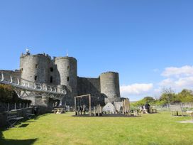 A castle with stone towers next to a playground and benches under a clear sky at Pen Y Bryn Bach in Harlech