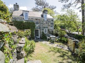 A stone cottage with a garden and outdoor table with chairs behind a wooden gate at Pen Y Bryn Bach in Harlech