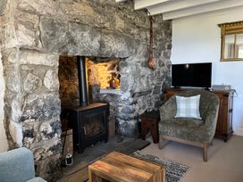 A room with a stone fireplace, a wood burning stove, an armchair with a cushion, a wooden cabinet with a TV on top and a wooden coffee table at Pen Y Bryn Bach in Harlech