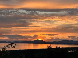 A sunset over a body of water with mountains in the background and some plants in the foreground at Pen Y Bryn Bach in Harlech