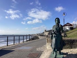 A statue by the sea with a path and buildings at Pebble Cove in Lyme Regis