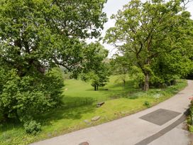 A view of a grassy area with trees and a winding road at Hollens Cottage in Grasmere