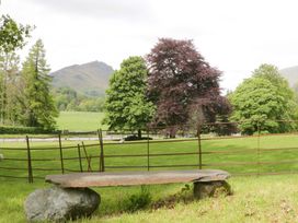 A bench surrounded by trees and a view of a mountain at Hollens Cottage in Grasmere