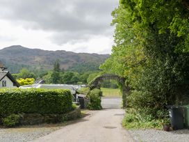 A driveway leading through an archway with trees and mountains at Hollens Cottage in Grasmere