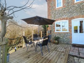 An outdoor deck with a table, four chairs, an umbrella, and a tree next to a stone and brick building at Cobble Cottage in Great Ryburgh