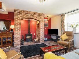 A living room with a brick fireplace wood stove leather chairs striped carpet and a television at Cobble Cottage in Great Ryburgh