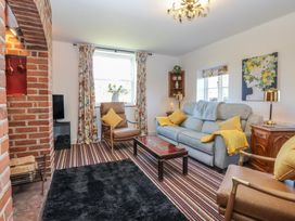 A living room with striped carpet a gray sofa two brown chairs a brick fireplace and floral curtains at Cobble Cottage in Great Ryburgh