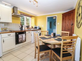 A kitchen with a round wooden dining table and chairs a large wall clock and yellow walls at Cobble Cottage in Great Ryburgh