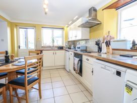 A kitchen with wooden countertops white cabinets a dining table with wooden chairs and tiled floor at Cobble Cottage in Great Ryburgh