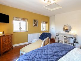 A bedroom with a bed a wooden dresser a chaise lounge a desk with a chair and two windows at Cobble Cottage in Great Ryburgh