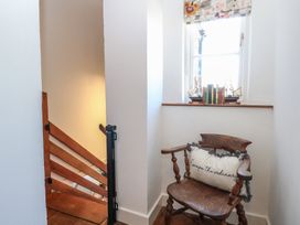 A wooden chair with a cushion reading escape the ordinary next to a window with model ships and books at Cobble Cottage in Great Ryburgh