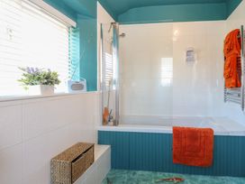 A bathroom with a bathtub and shower orange towels a plant and a radio on the windowsill at Cobble Cottage Great Ryburgh