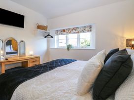 A bedroom with a bed with pillows a wooden dressing table with a mirror a wall-mounted television and a window with a floral blind at Cobble Cottage in Great Ryburgh