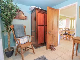 A room with a wooden chair, potted plant, wooden wardrobe, open door, and a dining area visible in the next room at Cobble Cottage Great Ryburgh