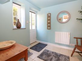 An entryway with a wooden table and chair two gray rugs a wall mirror and a white door at Cobble Cottage in Great Ryburgh
