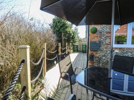 An outdoor deck with a glass table umbrella black chairs wooden posts with rope and bushes at Cobble Cottage in Great Ryburgh