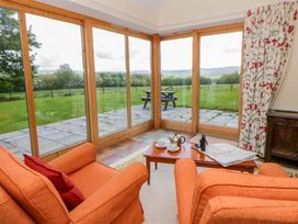 A conservatory with orange armchairs and a table with a tea set at Bryn Isaf near Swyddffynnon