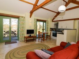 An open living room with a red sofa and pillows a round rug a TV on a wooden table a dining table with chairs and flowers and a kitchen area with cabinets and appliances at Cwtch in Swyddffynnon near Pontrhydfendigaid