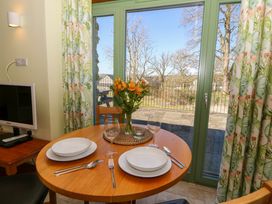 A dining area with a round wooden table set for two in front of green framed glass doors with floral curtains at Cwtch in Swyddffynnon near Pontrhydfendigaid