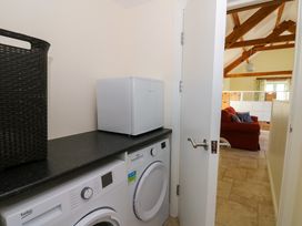 A utility room with washing machine dryer and mini fridge next to a door opening to a living room with a red sofa and wooden beams at Cwtch in Swyddffynnon near Pontrhydfendigaid