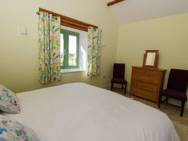 A bedroom with a bed white bedding two purple chairs wooden dresser with mirror and a window with green frame and floral curtains at Cwtch in Swyddffynnon near Pontrhydfendigaid