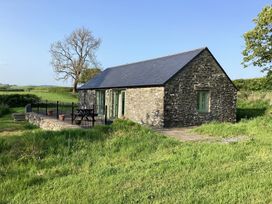 A stone cottage with a slate roof and a fenced patio with a picnic table in a grassy field at Cwtch in Swyddffynnon near Pontrhydfendigaid