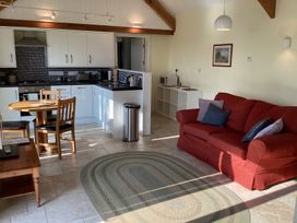 An open plan kitchen and living area with a red sofa a round wooden dining table and white kitchen cabinets at Cwtch in Swyddffynnon near Pontrhydfendigaid
