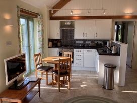 A kitchen with white cabinets a round wooden dining table with three chairs a television on a wooden table and a stainless steel trash bin at Cwtch in Swyddffynnon near Pontrhydfendigaid