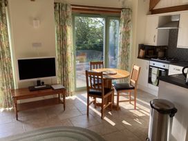 A kitchen and dining area with a round wooden table and chairs a small television on a wooden table drawers oven and stove visible and large windows with floral curtains at Cwtch in Swyddffynnon near Pontrhydfendigaid