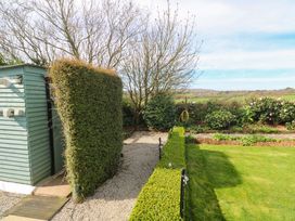 A garden with a shed, hedge, and flower beds at Higher Merther Farm Shepherds Hut Helston