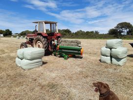 A tractor and baler in a field with hay bales at Higher Merther Farm Shepherds Hut Sithney near Helston
