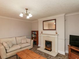 A living room with a beige sofa a wooden bookshelf a fireplace with a mirror above and a TV on a wooden stand at Bellmanear Farm Cottage in North Grimston near Malton
