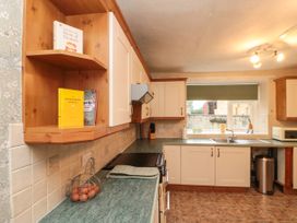 A kitchen with white cabinets green countertops a window over the sink and cookbooks on a wooden shelf at Bellmanear Farm Cottage in North Grimston near Malton