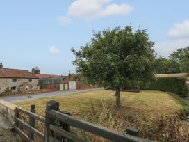 A grassy area with a tree and a wooden fence near stone and brick buildings at Bellmanear Farm Cottage in North Grimston near Malton