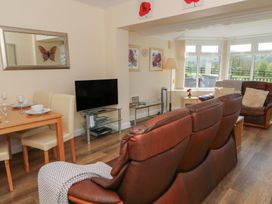 A living room with brown leather sofas a dining table with cream chairs a television and large windows at Trem-Yr-Afon in Aberaeron