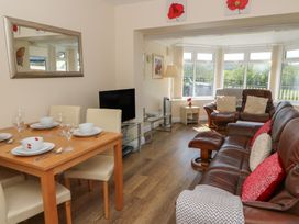 A living and dining area with a wooden dining table set with dishes and glasses a brown leather sofa set a television on a glass stand and windows showing an outdoor view at Trem-Yr-Afon in Aberaeron