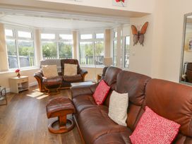 A living room with brown leather sofas red and white cushions wooden floor and large windows at Trem-Yr-Afon in Aberaeron
