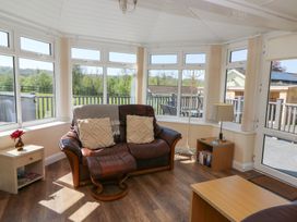 A sunroom with a leather armchair two cushions a side table with a lamp and books at Trem-Yr-Afon in Aberaeron