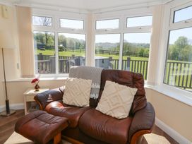 A sitting area with a brown leather chair and ottoman near large windows overlooking a fenced grassy yard at Trem-Yr-Afon in Aberaeron