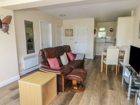 A living area with a brown leather sofa and matching footstool a wooden side table a dining table with four chairs and a kitchen area at Trem-Yr-Afon in Aberaeron