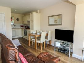 An open plan living area with brown leather sofas a wooden dining table with four chairs a kitchen area and a television on a glass stand at Trem-Yr-Afon in Aberaeron