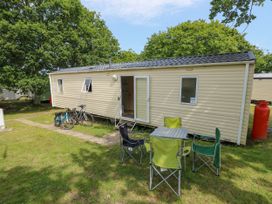 A mobile home with an open door bicycles parked outside and outdoor table with four chairs on grass at Greenwood in Cowes