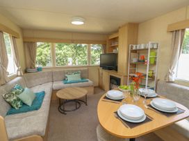 A living area with a dining table set for four and an L-shaped sofa with cushions at Greenwood in Cowes