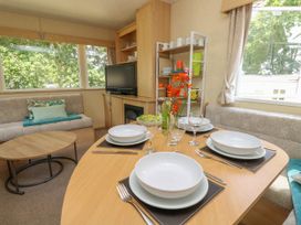 A dining table set with plates glasses cutlery and a flower vase beside a sofa and a television in a living area at Greenwood in Cowes