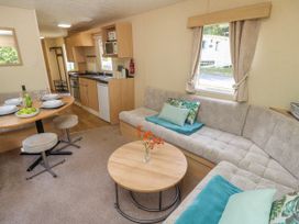 A living area with an L-shaped sofa and coffee table next to a dining table with place settings and stools and a kitchen with wooden cabinets at Greenwood in Cowes