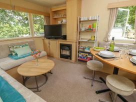 A living area with a sofa and cushions a coffee table with flowers a TV and fireplace a dining table set with plates glasses and wine at Greenwood in Cowes